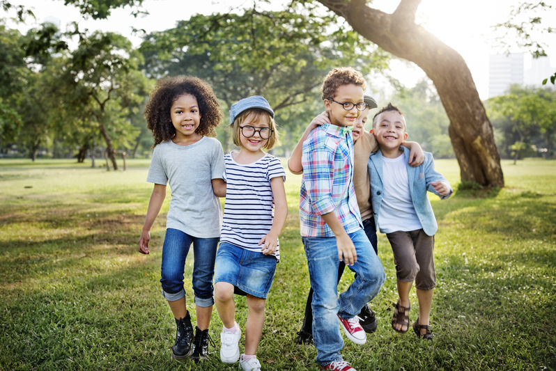 Kinder spielen auf einer grünen Wiese unter einem Baum. 